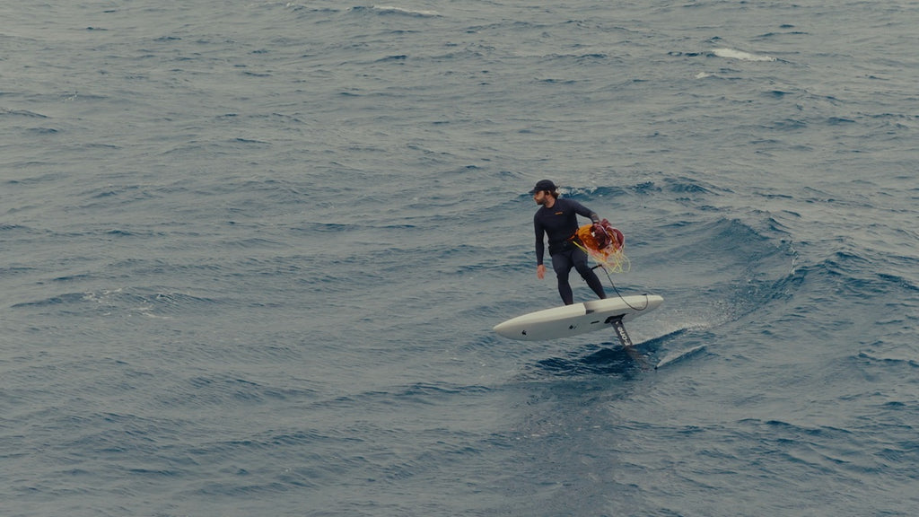 Foiler surf einer Welle mit gepacktem F-ONE Frigate in der Hand