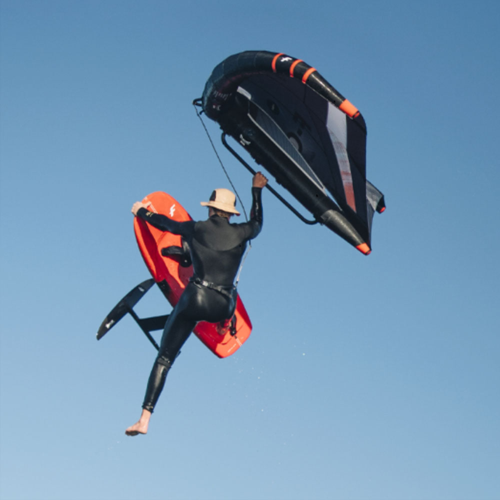 Wingfoiler springt mit und hält Wing mit einer Hand am Carbon Boom 