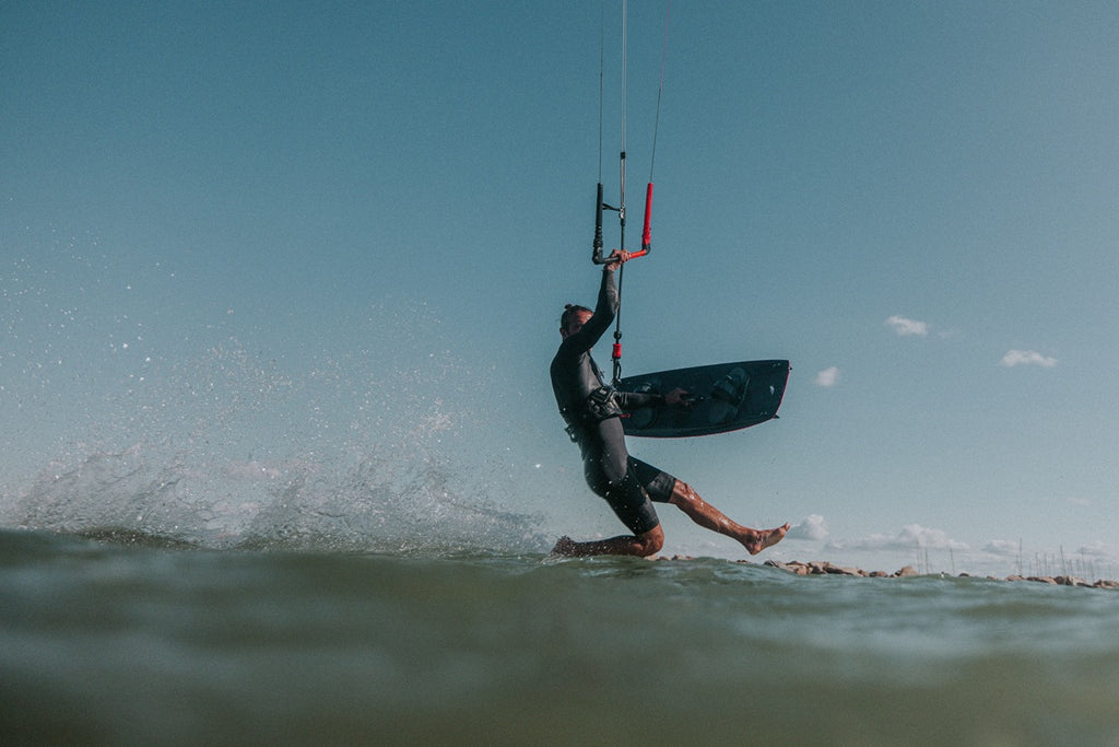 Kiterläuft über das Wasser und hält das F-ONE Spark Hybrid in der Hand während man das Board von der Oberseite sieht